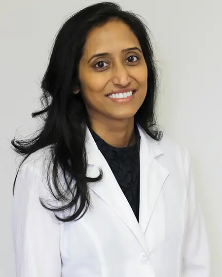 Dr. Anupama Vurugonda, dentist at Midwest Family Dental Care, smiling in a white coat, showcasing her expertise in family and cosmetic dentistry.