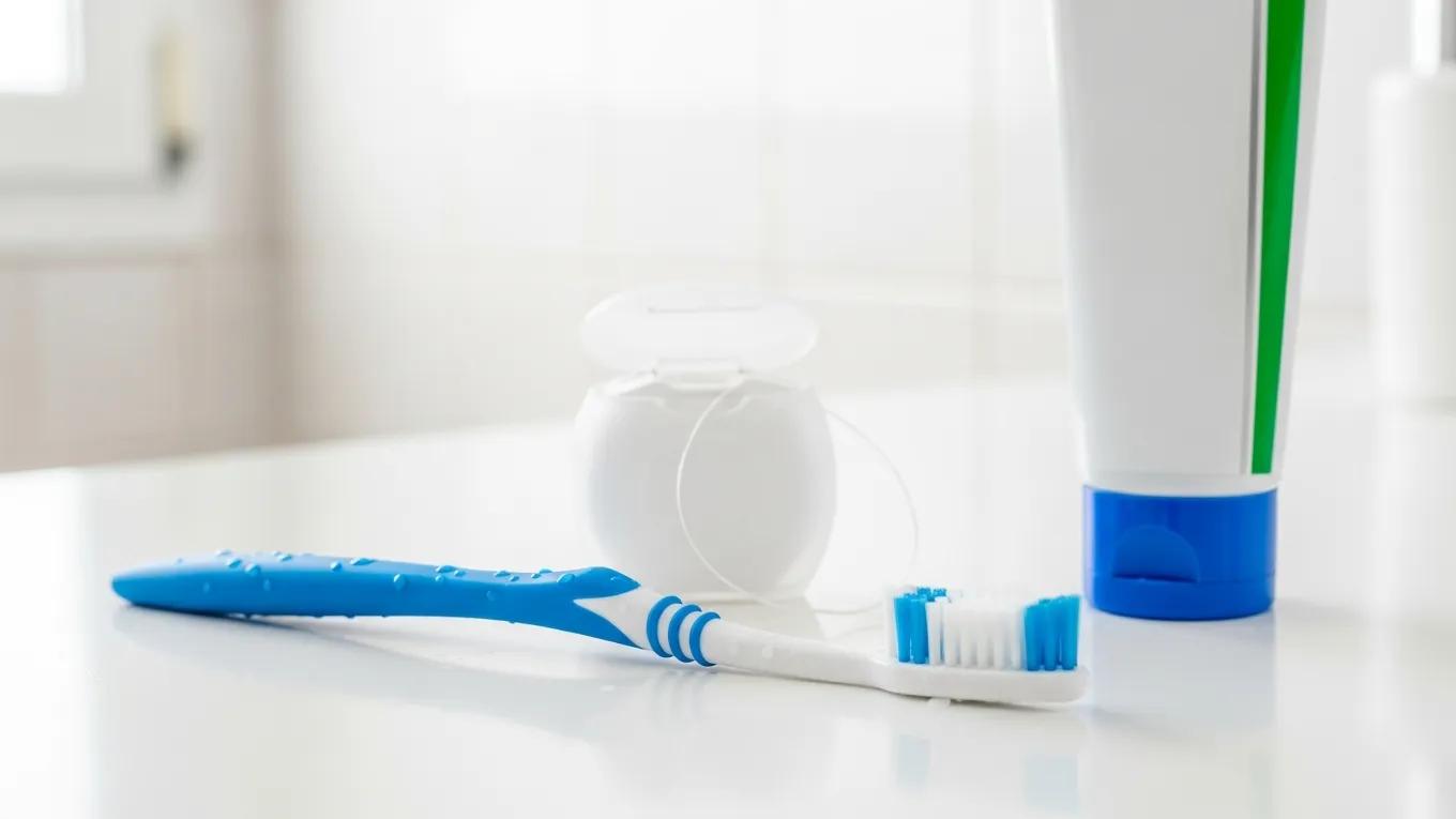 Toothbrush, dental floss, and toothpaste on a bathroom counter, representing daily oral hygiene for gum health